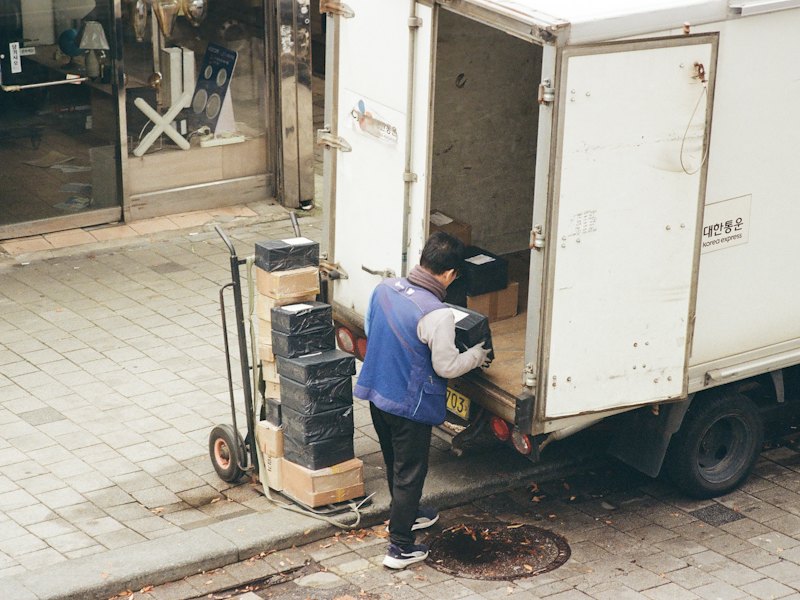 トラックの荷台から段ボール箱を台車に降ろすドライバー
